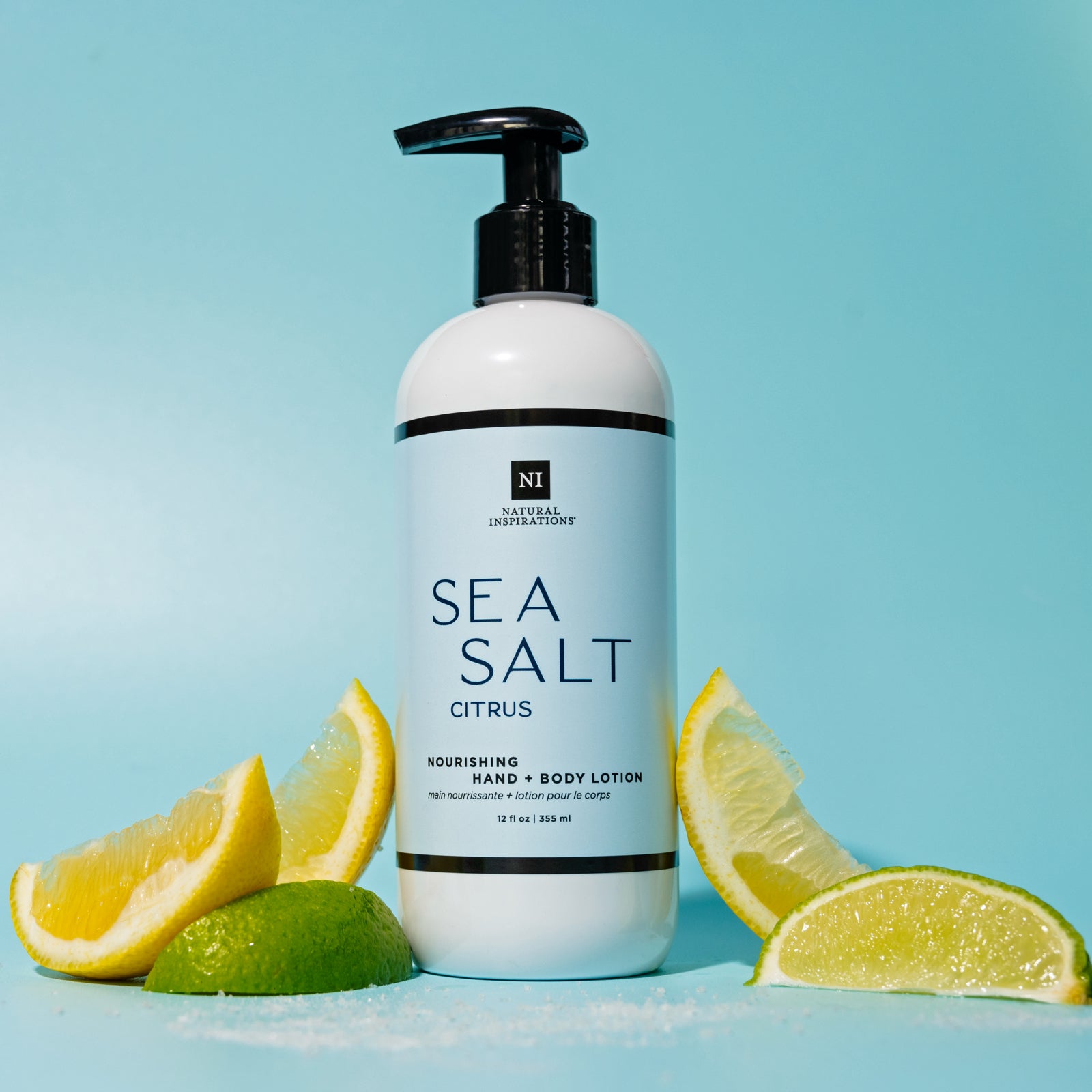 Sea Salt Citrus Nourishing Hand and Body Lotion on a blue background with Lemons, Limes and sea salt scattered around it.