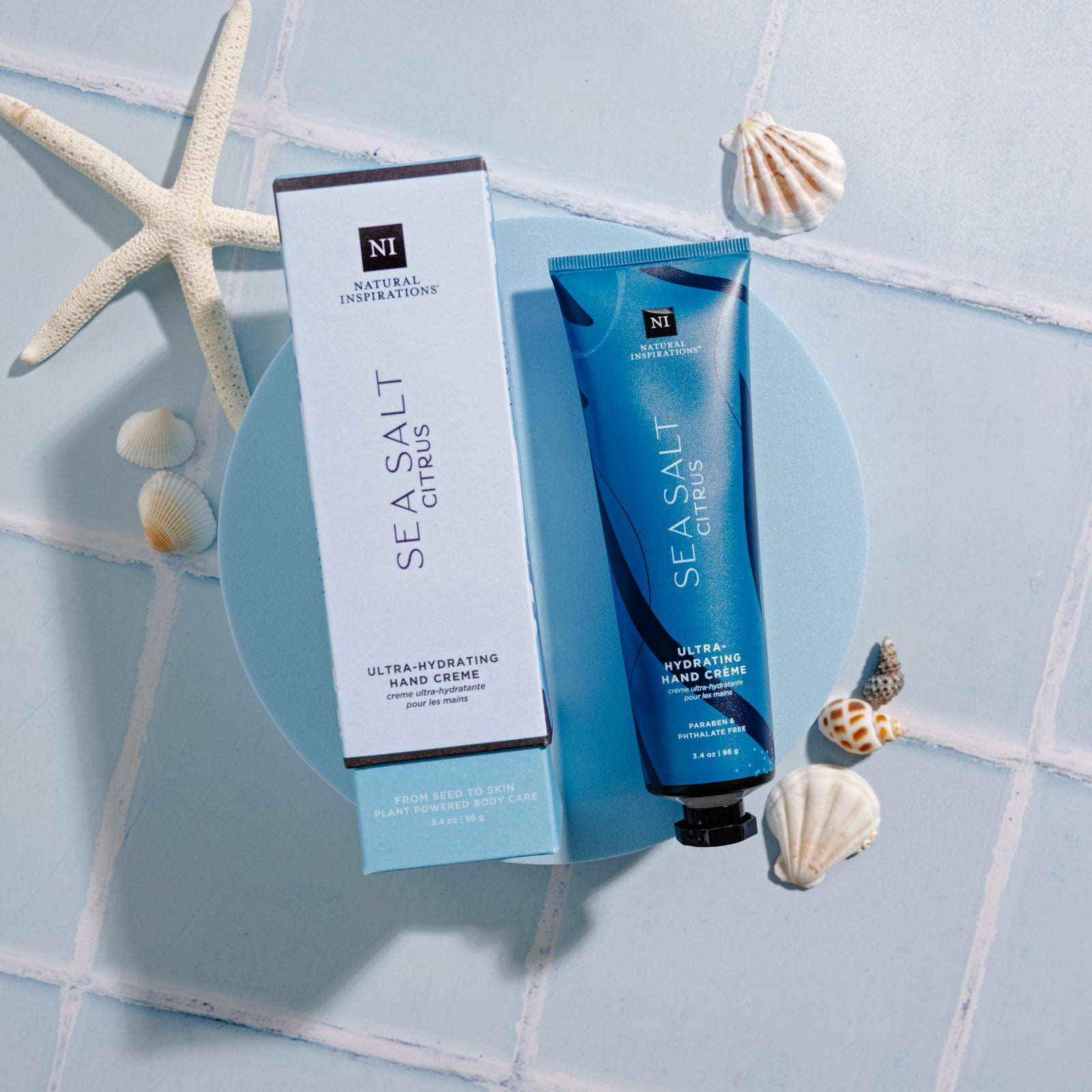 overhead view of Sea Salt Citrus boxed Hand Cream on a blue tile background with sea shells and a starfish scattered around it.