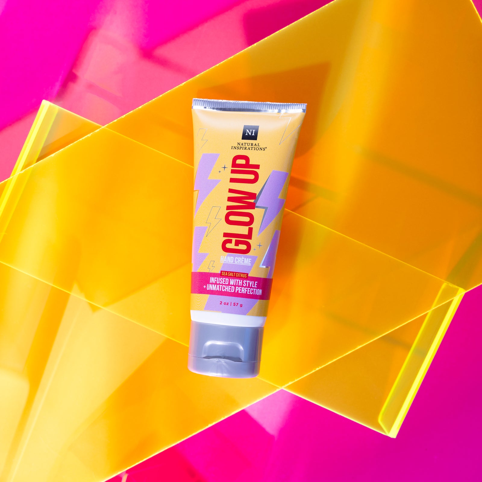 close up of glow up mini hand cream on a pink background with yellow neon props