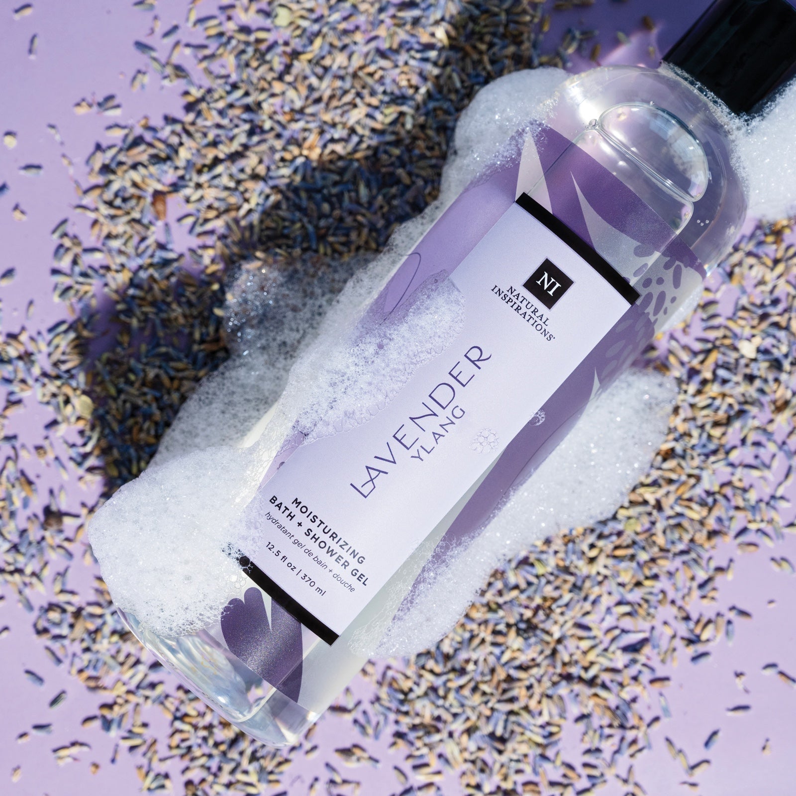 overhead view of lavender ylang moisturizing bath and shower gel on lavender seeds with suds covering the bottle