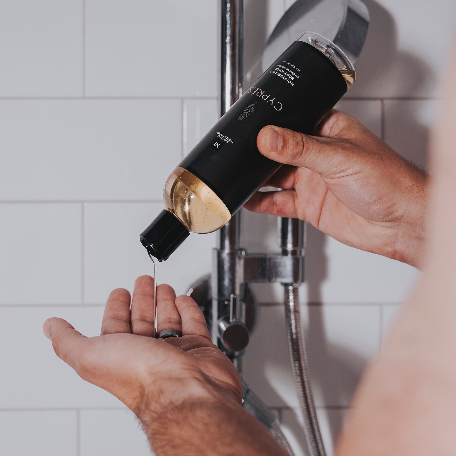close up of a man pouring cypres moisturizing body wash into his hand in the shower