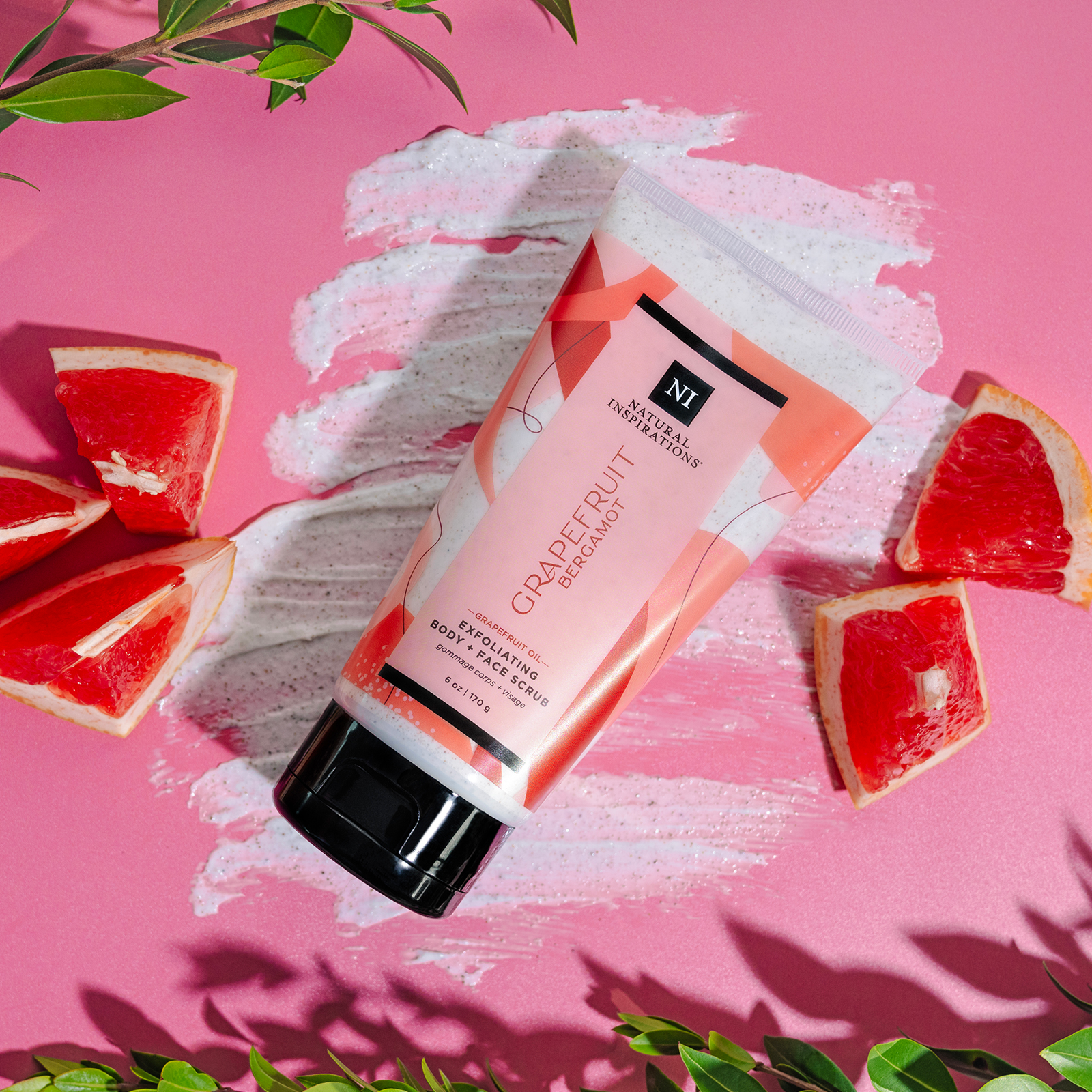 overhead view of grapefruit bergamot body and face scrub on a pink background with green nature cues and slices of grapefruit