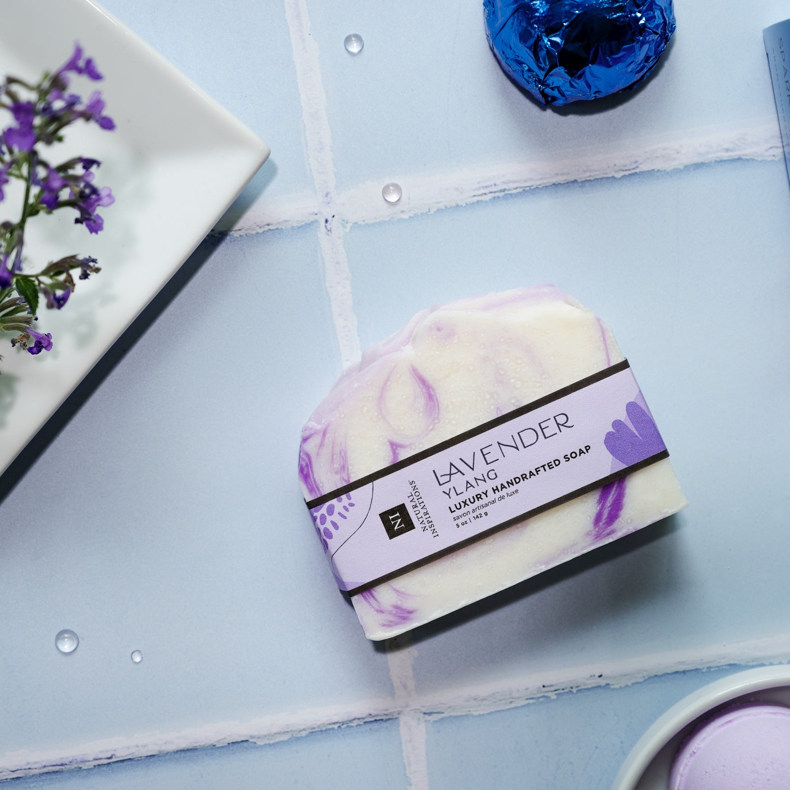 overhead view of lavender ylang handcrafted bar soap on a blue tile background
