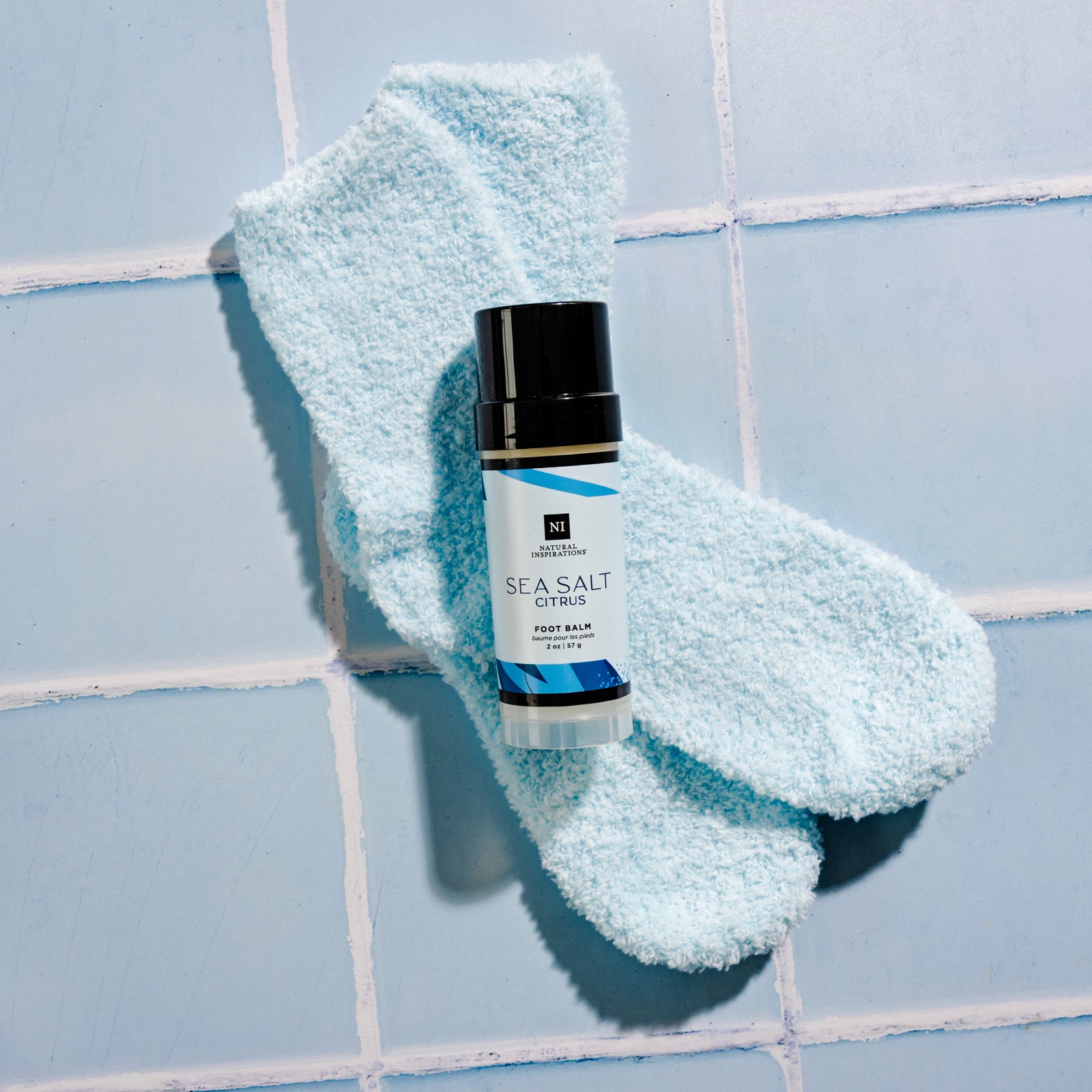 Overhead view of blue Sock Cozies and Sea Salt Citrus Foot Balm on a blue tile background