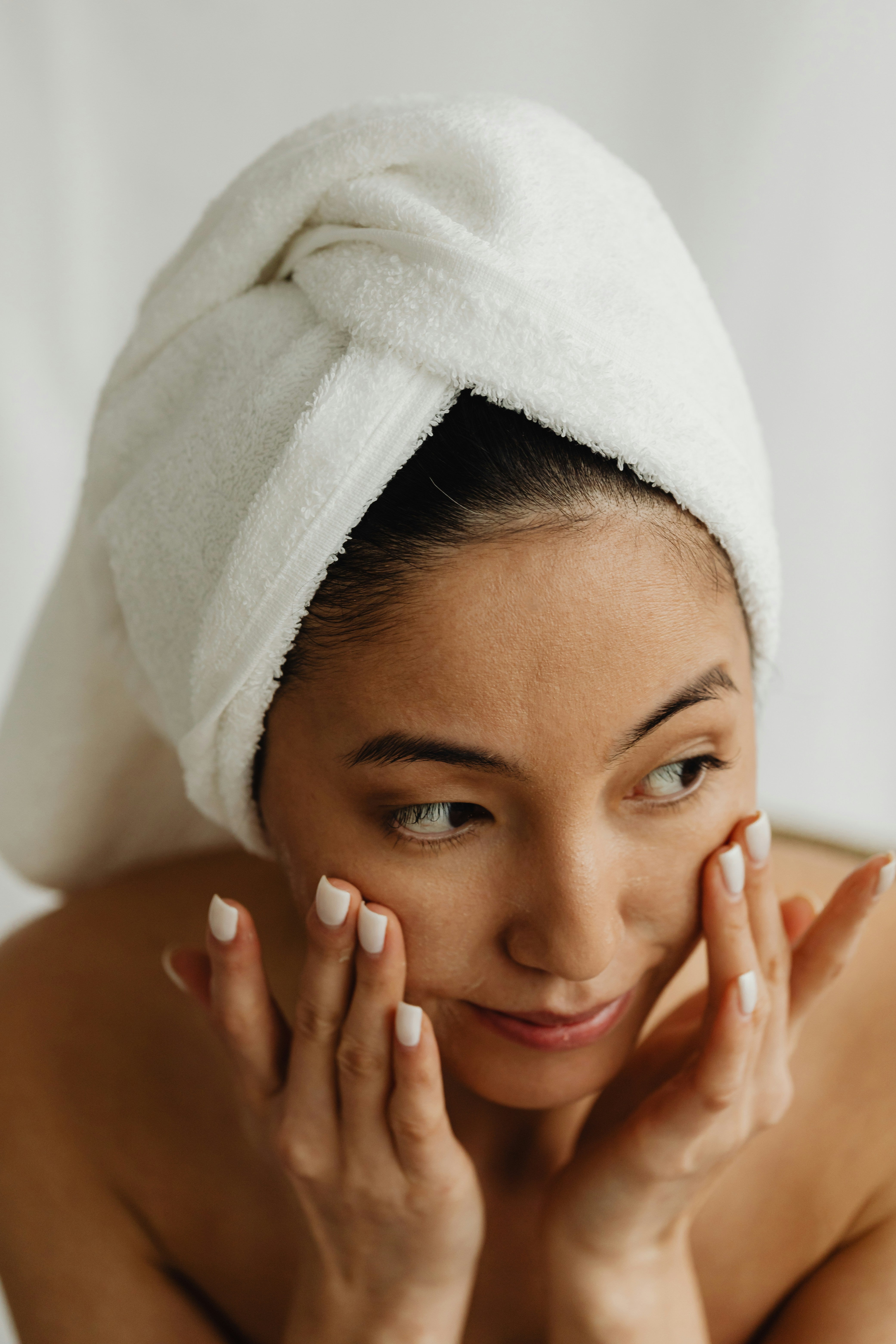 close up of a woman with her hair pulled up in a towel, touching her face
