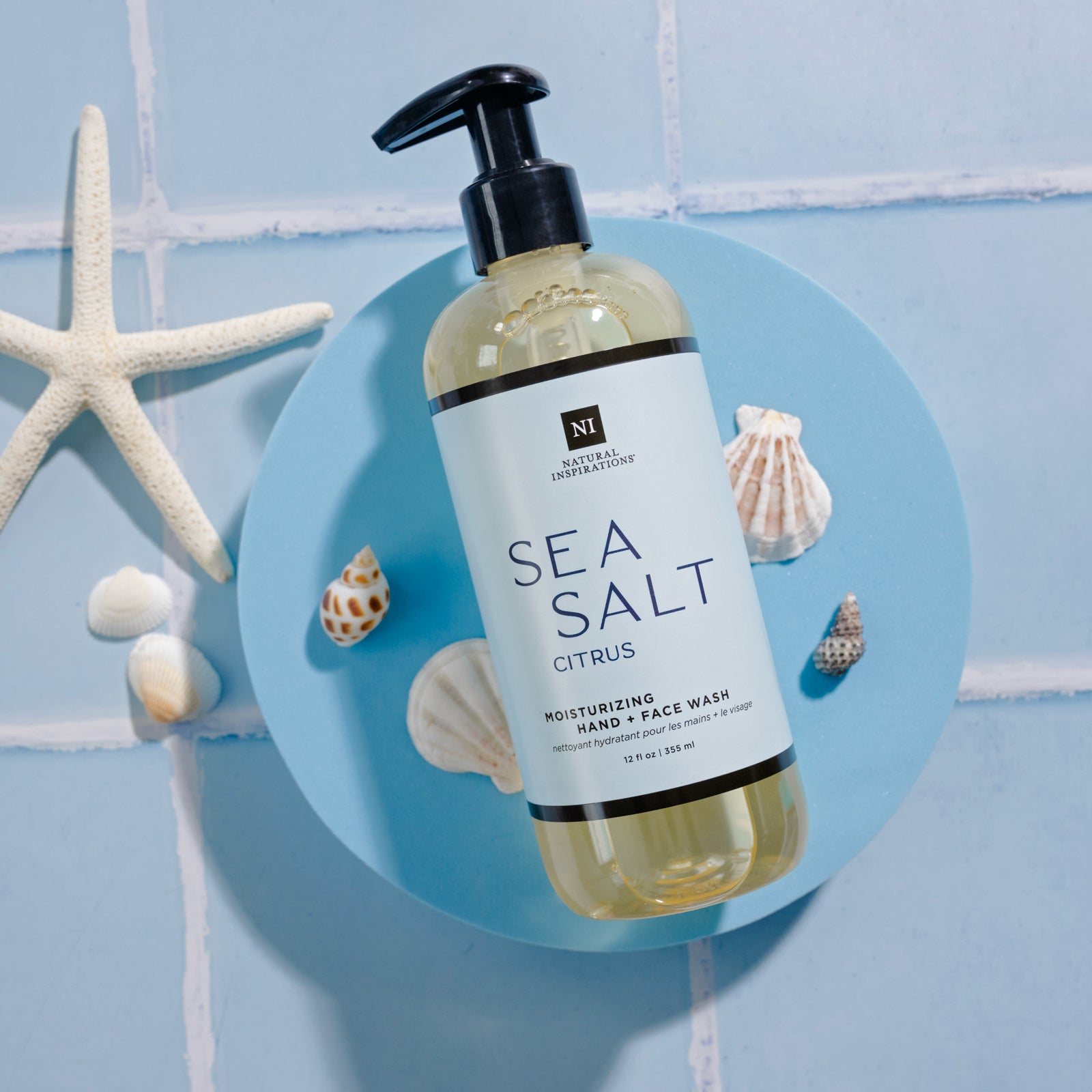 overhead view of Sea Salt Citrus Moisturizing Hand and Face Wash on a blue tile background with seashells and a starfish scattered in the background