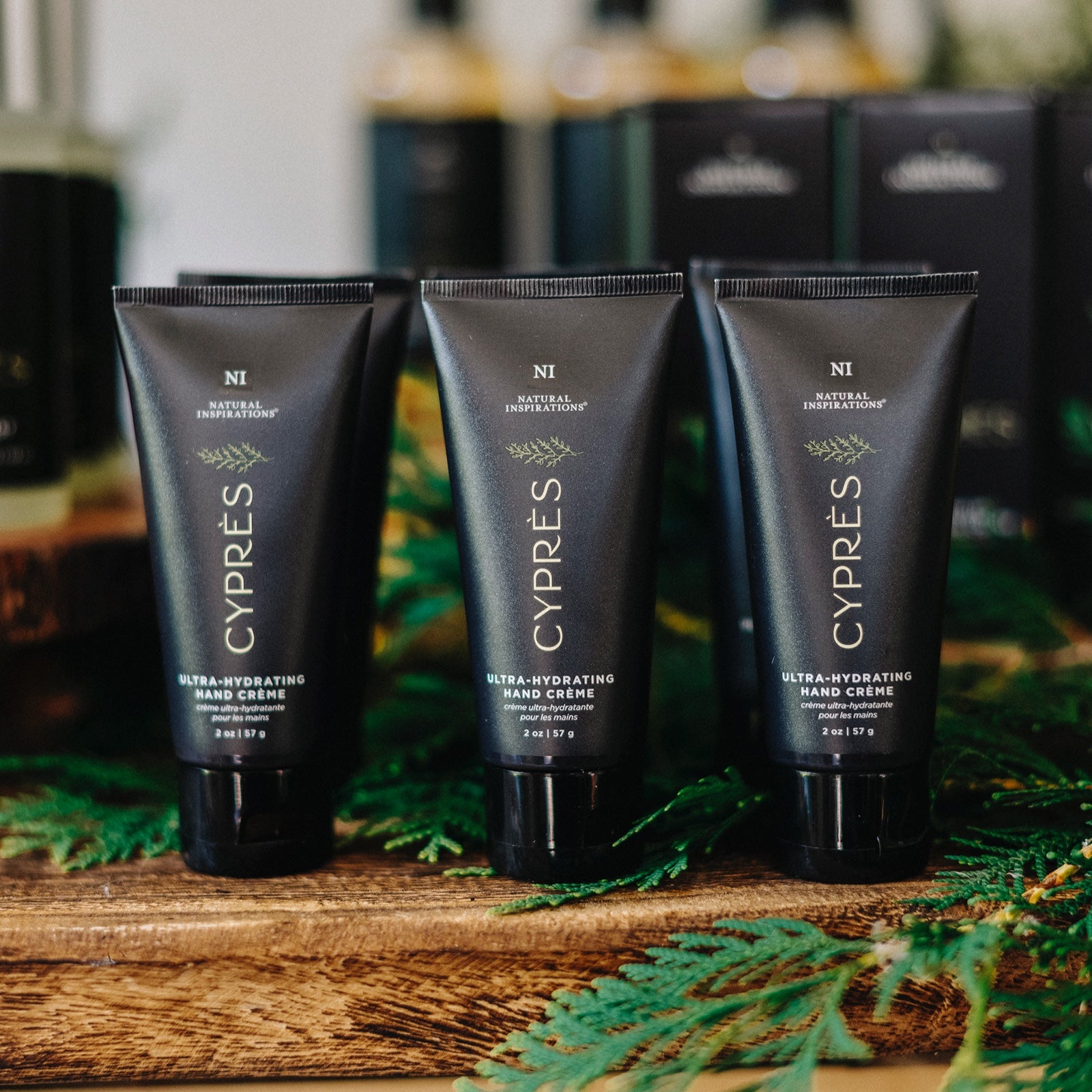 close up of cypres mini hand creams on a wood table with cypress branches scattered throughout