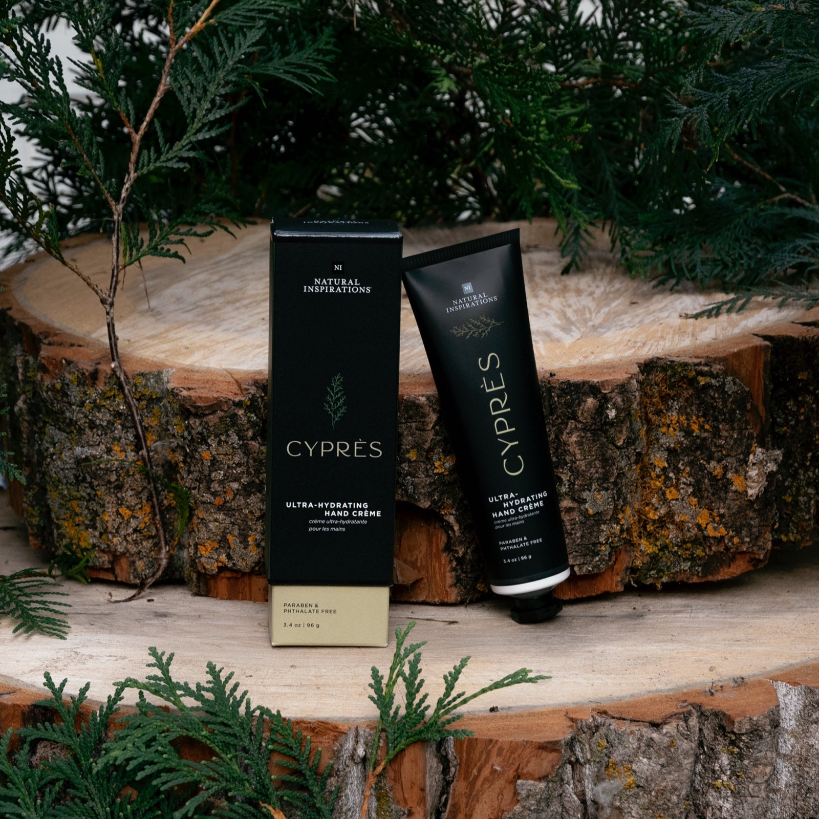 close up of cypres 3.4 oz hand cream sitting on top of a stack of sliced logs with cypress trees scattered throughout