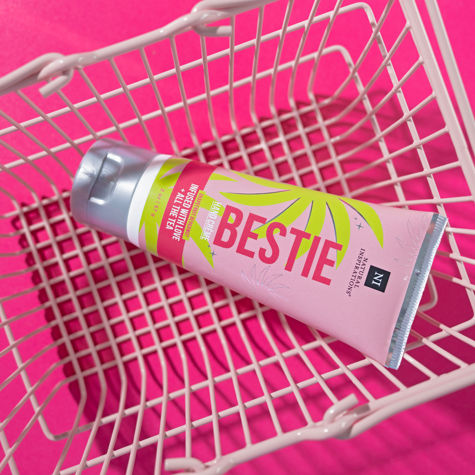 overhead view of bestie mini hand cream in a small pink shopping basket on a hot pink background