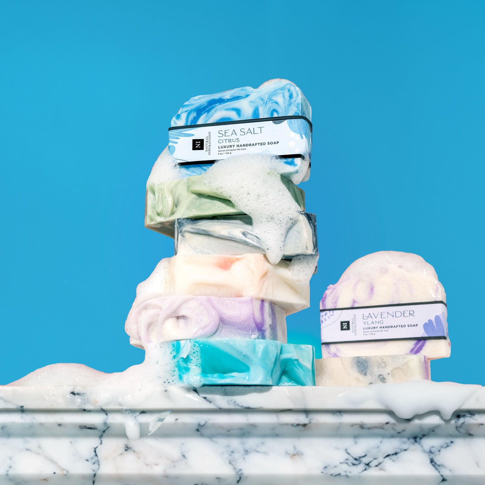 stack of handcrafted bar soaps on a marble surface covered in sudsy bubbles
