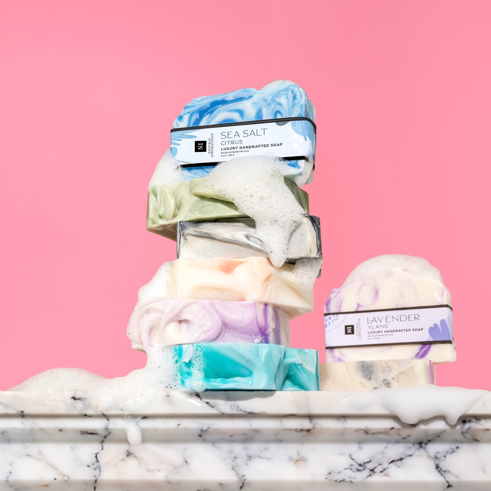 stack of handcrafted bar soaps on a marble surface covered in sudsy bubbles
