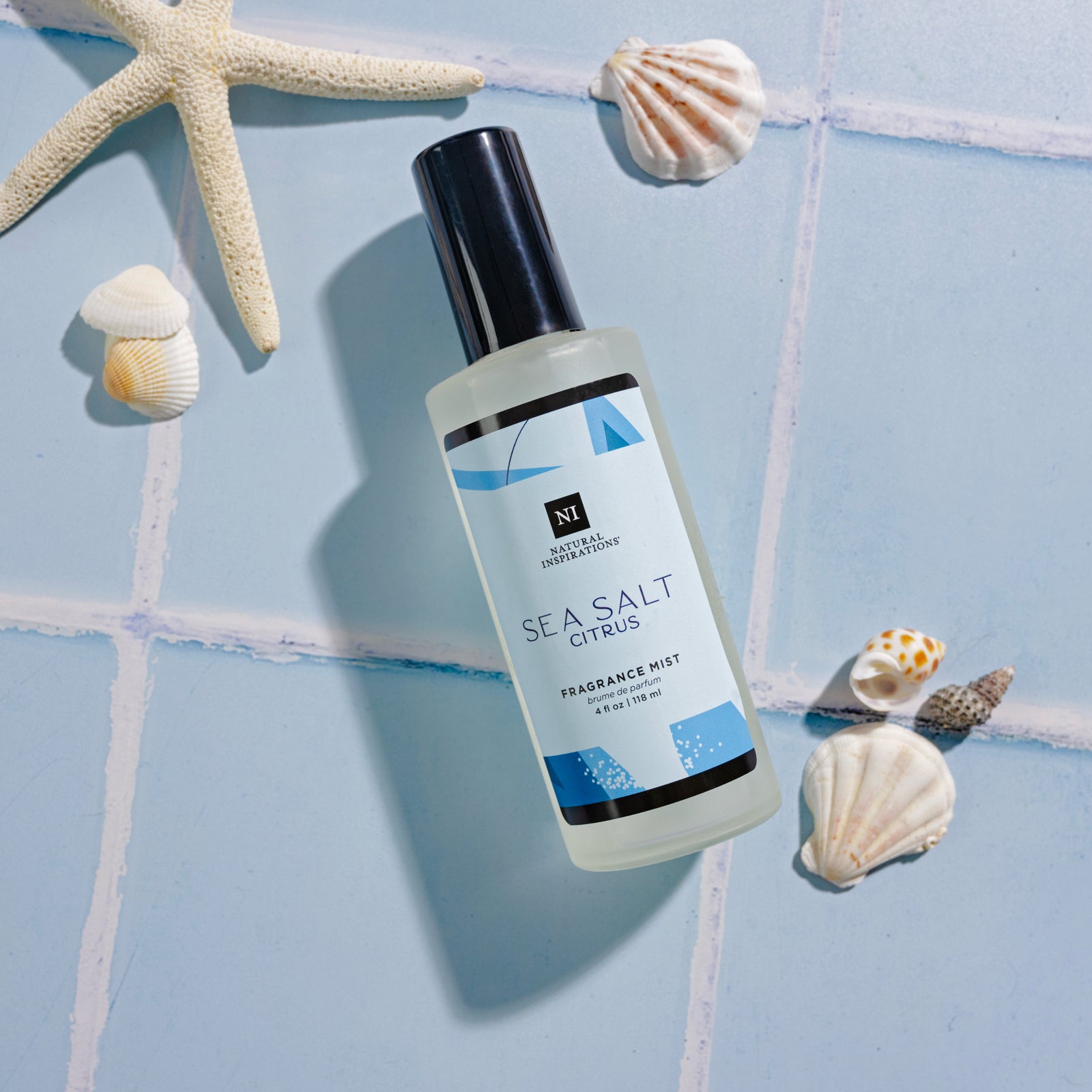 overhead view of Sea Salt Citrus Fragrance Mist on a blue tile background with seashells and a starfish scattered in the background