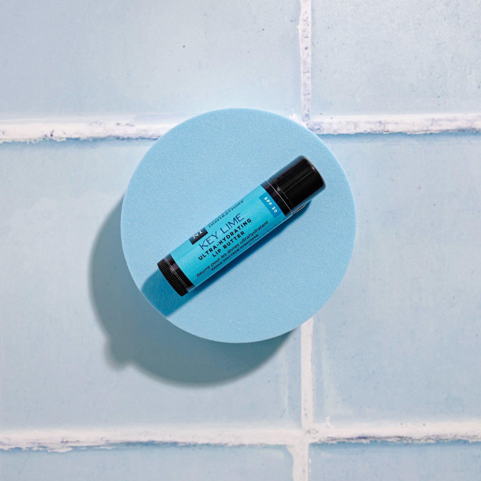 Overhead view of Key Lime flavored Lip Butter on a blue tile background