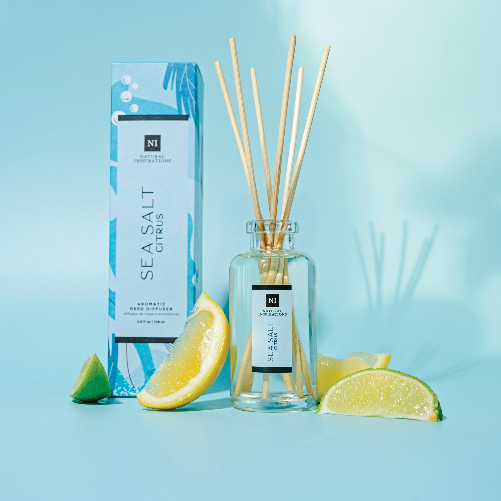 sea salt citrus aromatic reed diffuser on a blue background with lemons and limes scattered throughout
