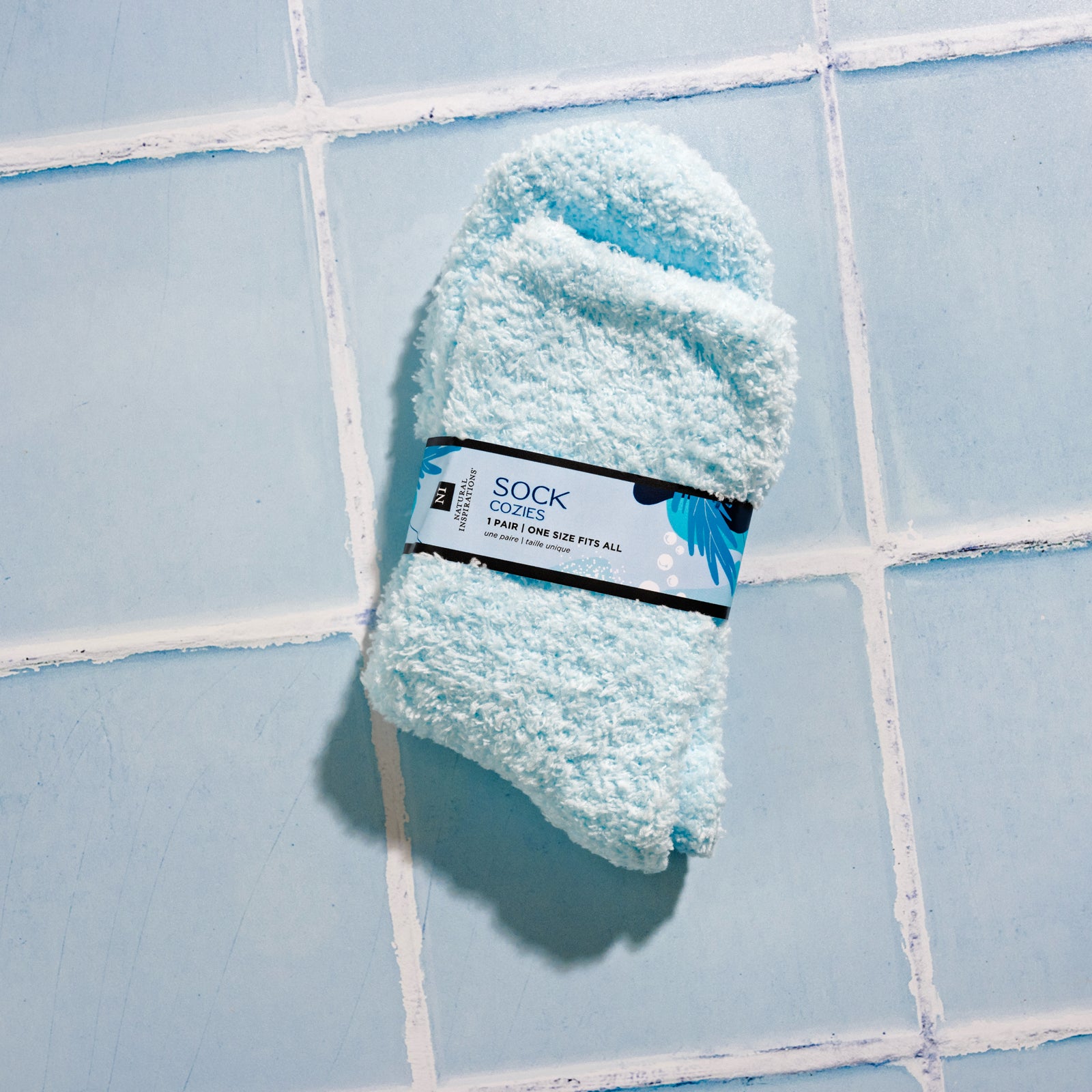 Overhead view of blue Sock Cozies that come in the Sea Salt Citrus Foot Therapy Kit on a blue tile background
