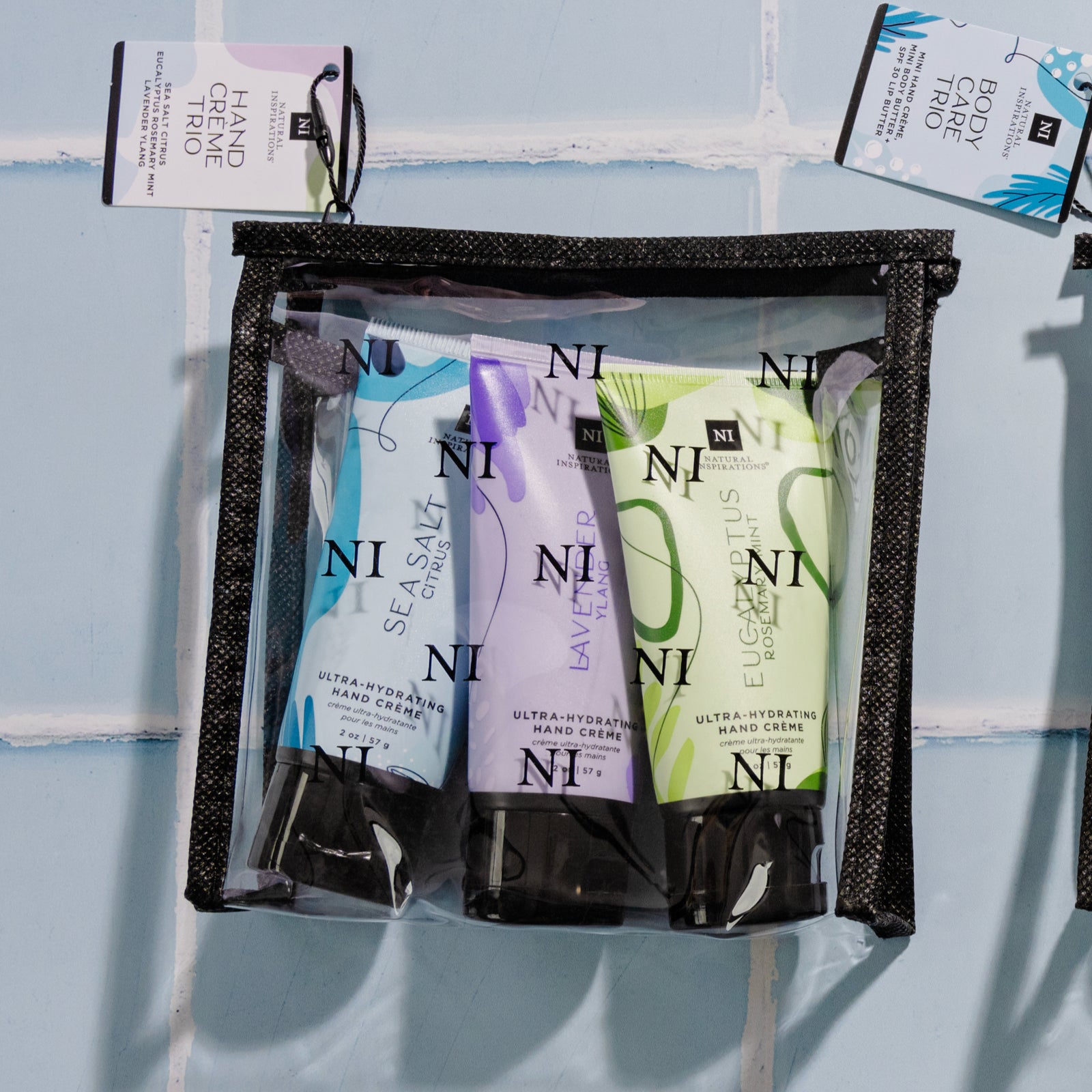 overhead view of the natural inspirations mini hand cream trio in a reusable clear NI travel bag on a blue tile background