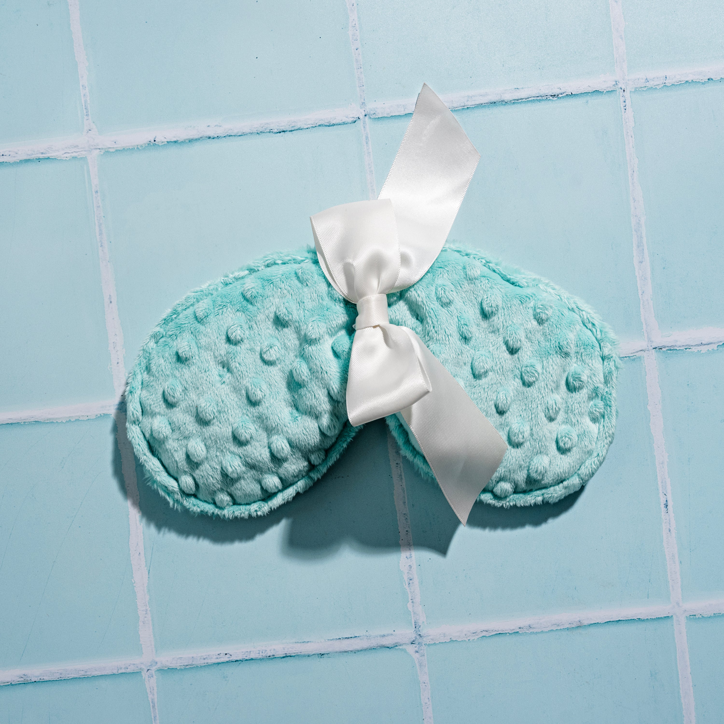 overhead view of an Agave Pear Relaxing Eye Pillow on a blue tile background